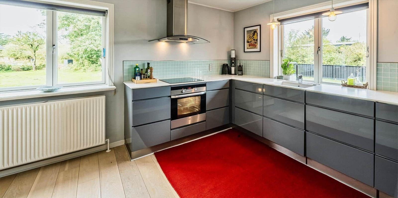 Moderne Küche mit grauen Schränken, rotem Teppich und Fenstern mit Blick auf Garten.
