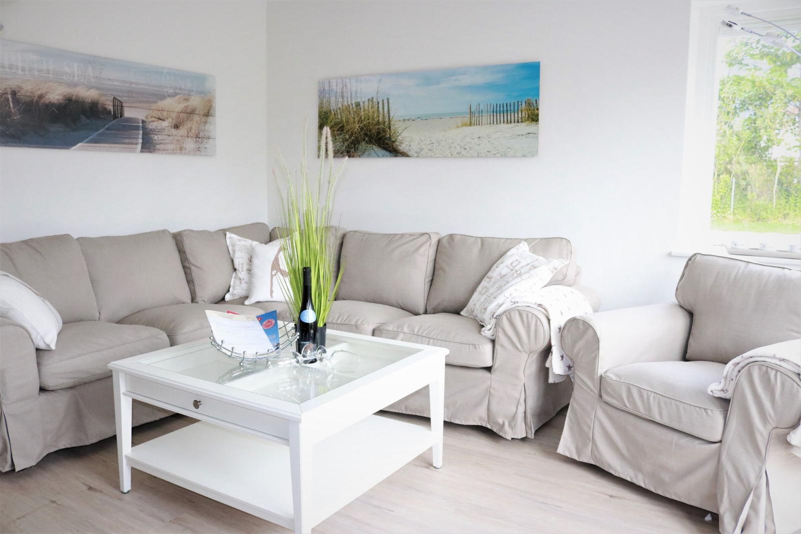Wohnzimmer mit Sofa, Sessel und Tisch. Wandbilder zeigen Strand.