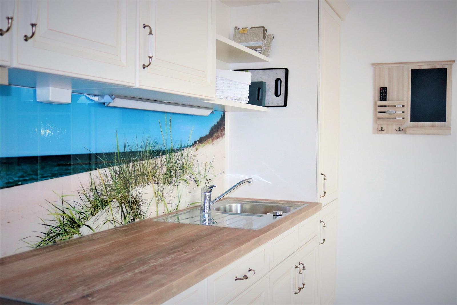 Küche mit Küchenzeile, Spüle und Küchenrückwand mit Strandmotiv.