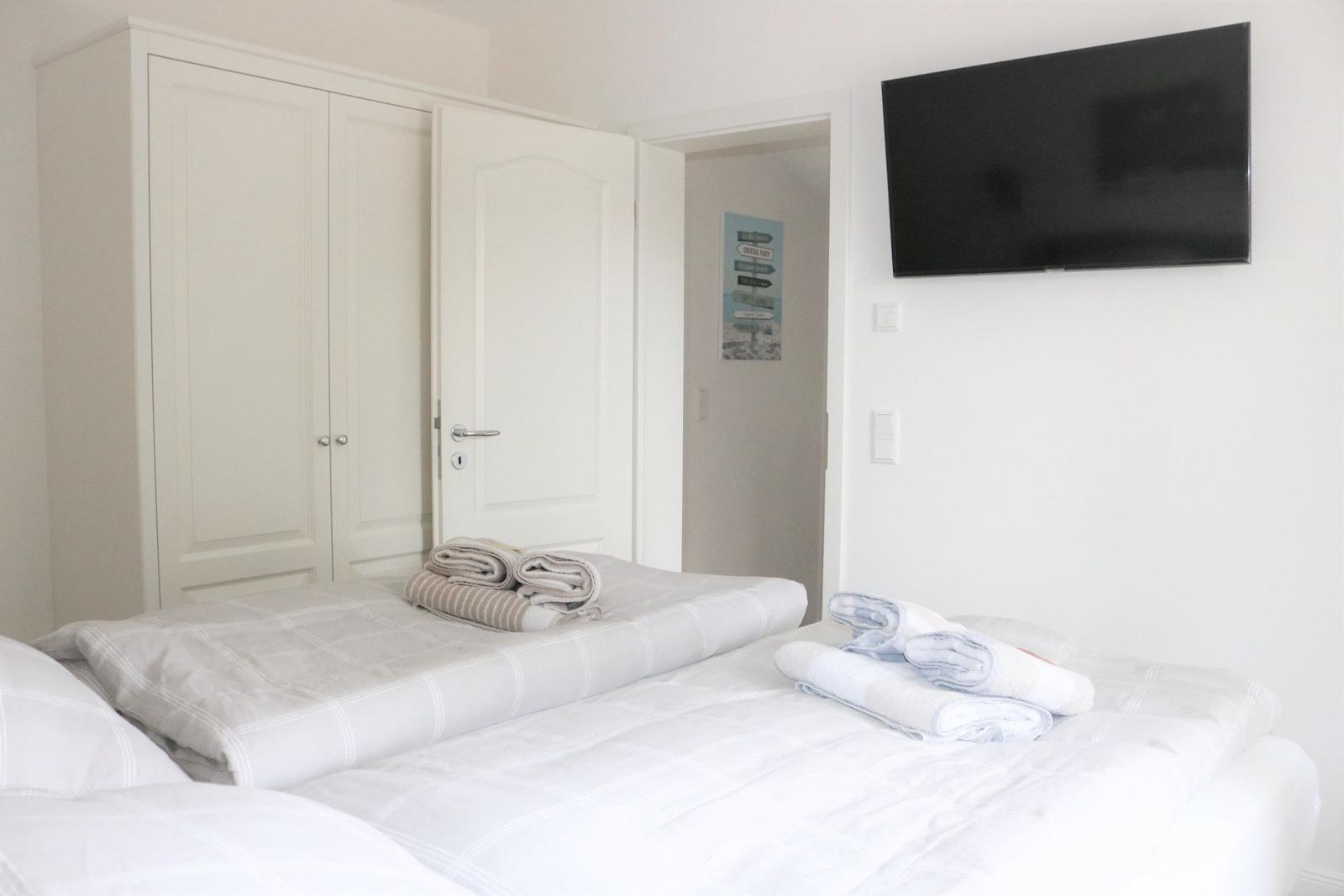 Schlafzimmer mit Bett, Kleiderschrank und Wandfernseher.