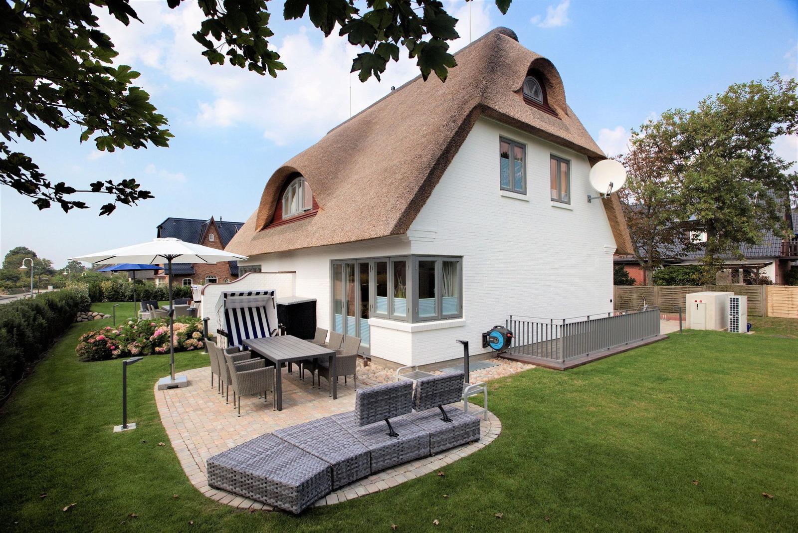 Wohnhaus mit Dach aus Stroh, Terrasse und Gartenbereich mit Sitzmöbeln.