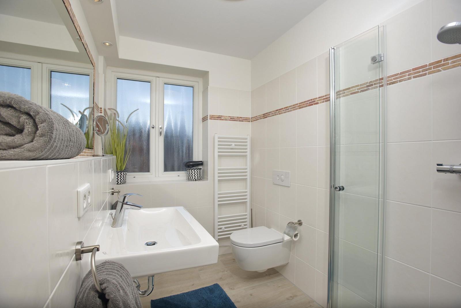 Badezimmer mit Dusche, Waschbecken und Toilette. Fenster und Handtuchhalter sichtbar.