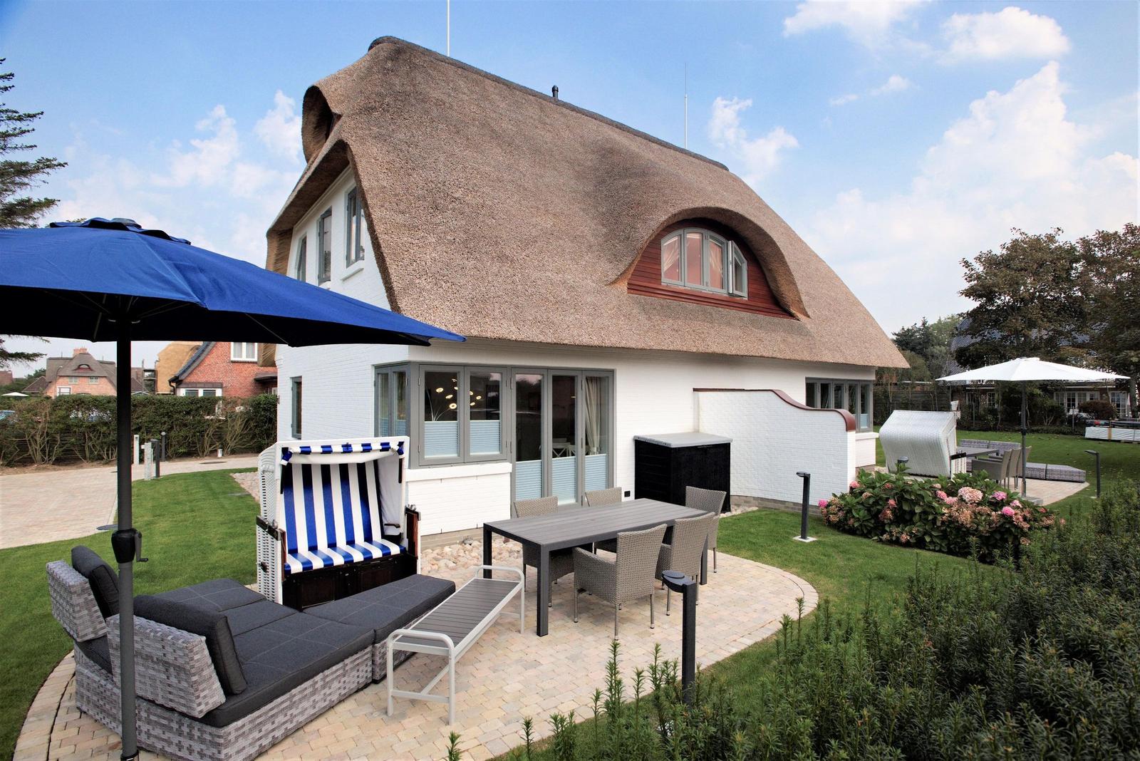 Haus mit strohgedecktem Dach und großem Gartenbereich mit Sitzmöbeln.