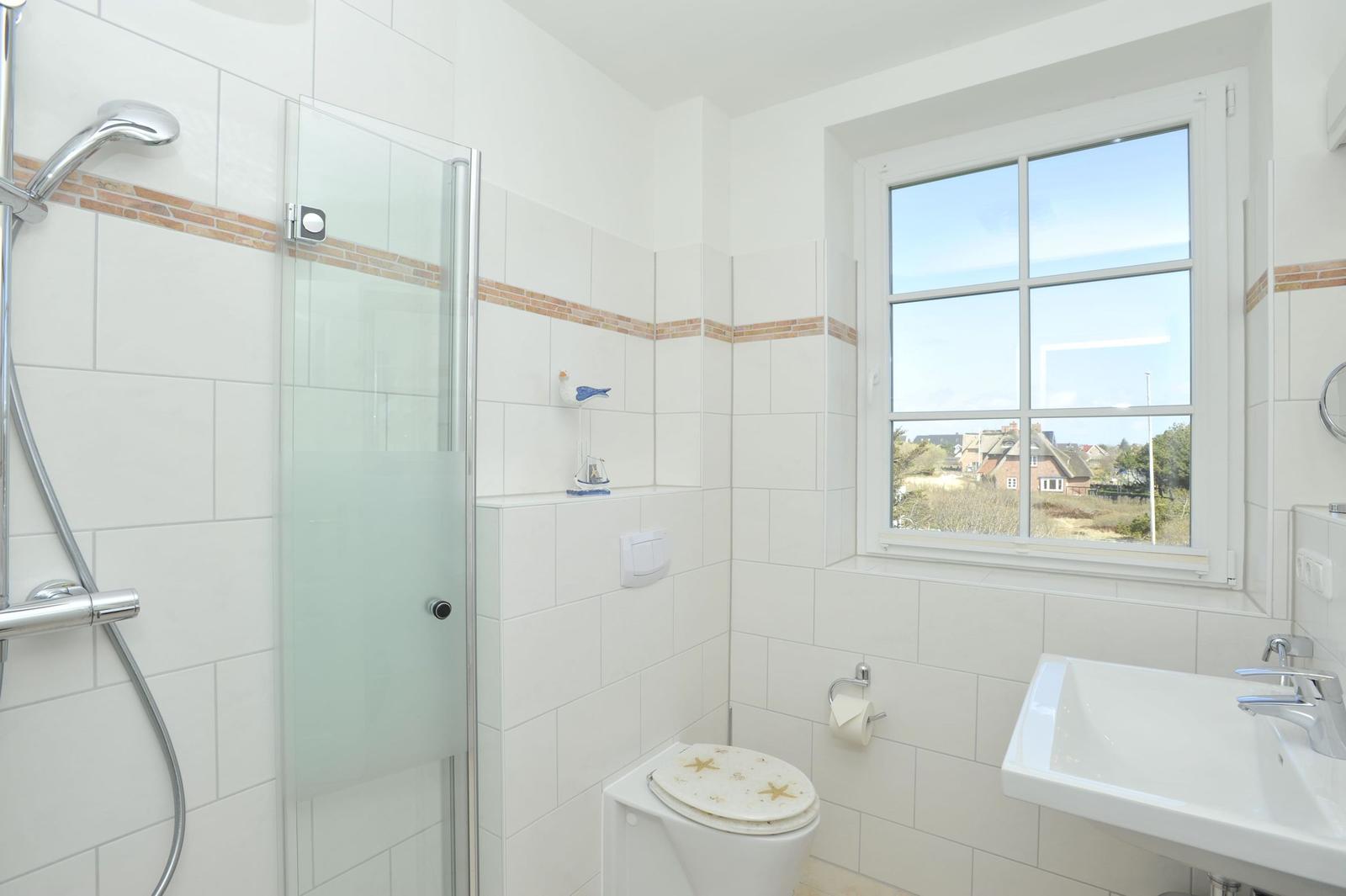 Badezimmer mit Dusche, Toilette und Waschbecken. Fenster mit Blick auf Außenbereich.