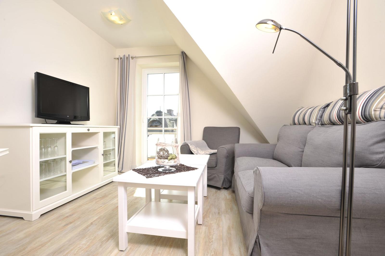 Wohnzimmer mit Sofa, Sessel, TV und Fenster
