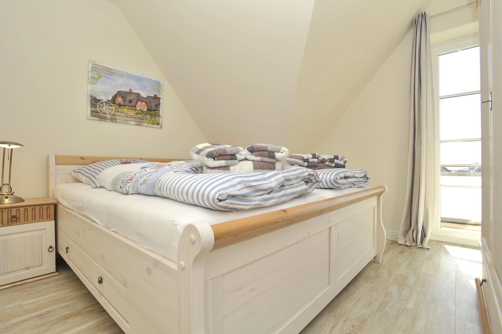 Schlafzimmer mit Dachschrägen, Bett, Nachttisch und Fenster.