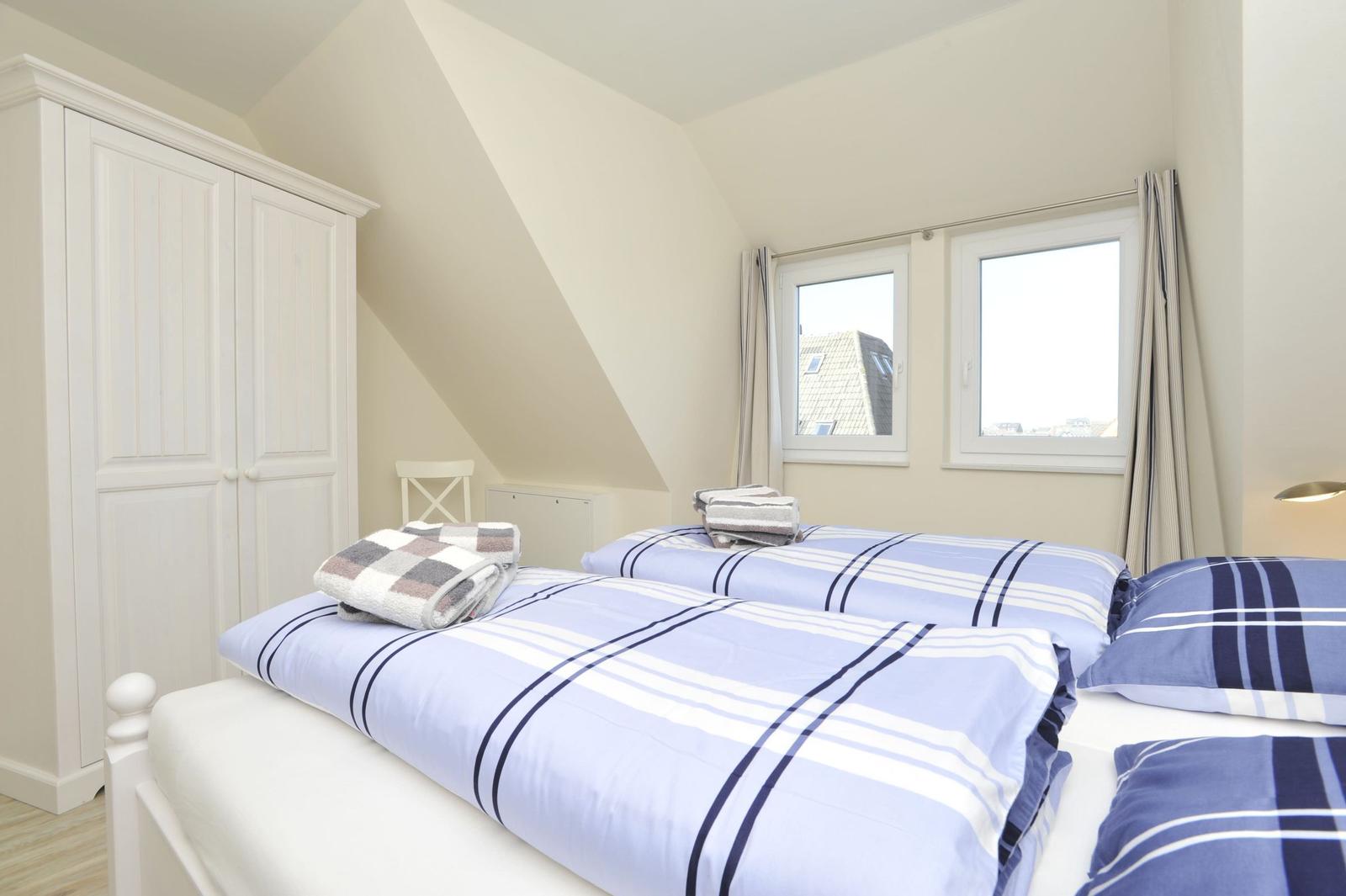 Zimmer mit Doppelbett, Kleiderschrank und Fenstern mit Blick auf Dächer.