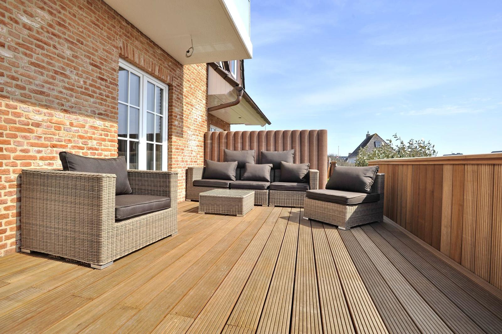 Terrasse mit Sitzgruppe, Holzdielen und Backsteinwand. Blick auf den Himmel.