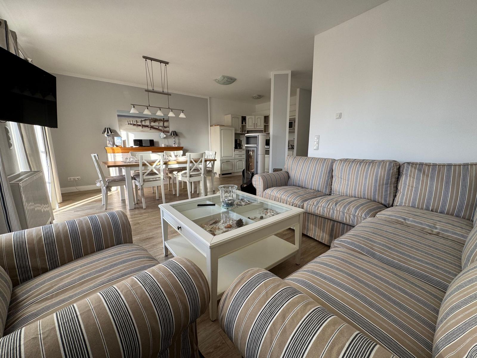 Wohnzimmer mit Sofa, Esstisch und Küche im Hintergrund.