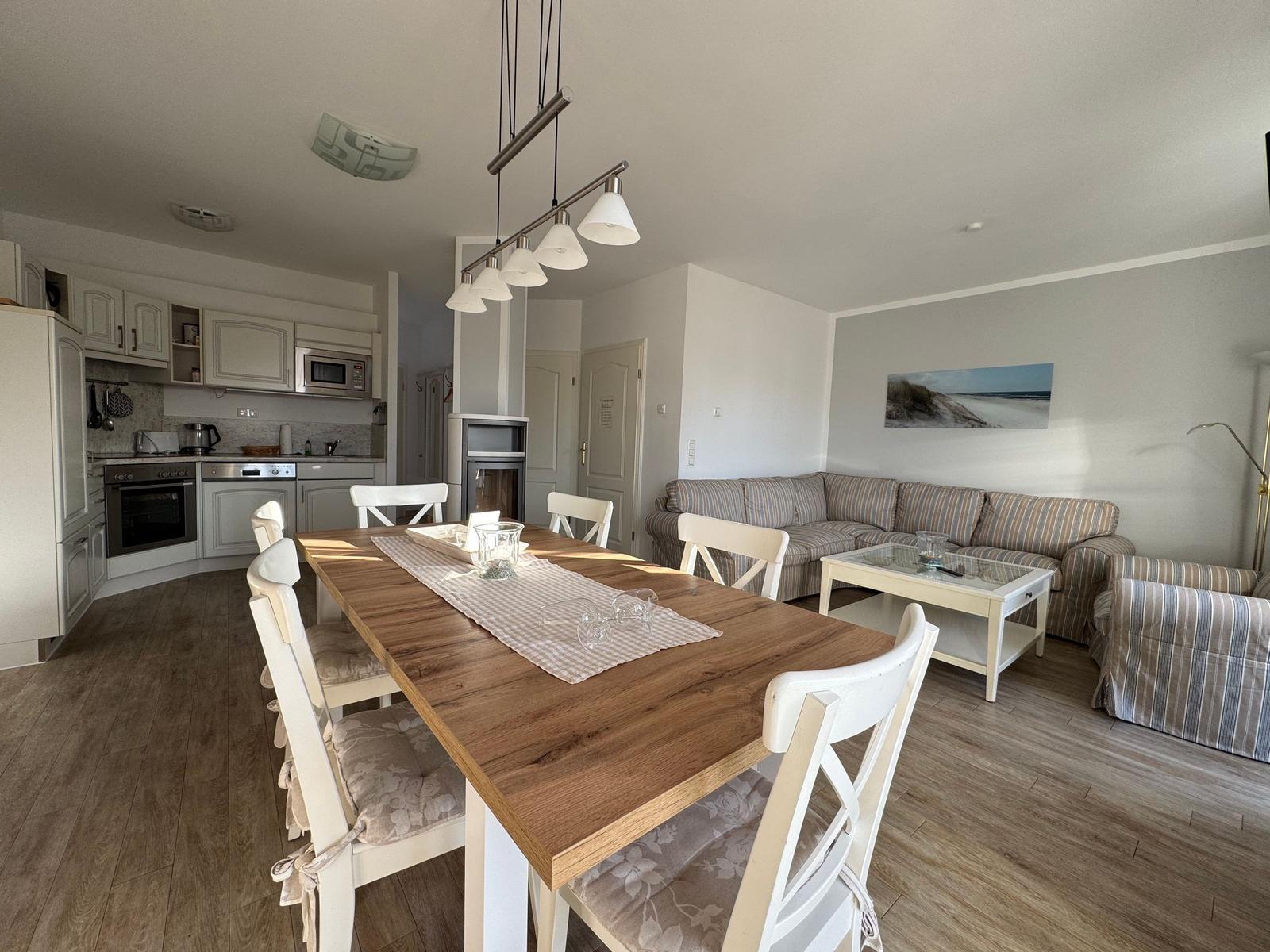 Essbereich mit Tisch und Stühlen, Küche und Wohnzimmer mit Sofa und Couchtisch.