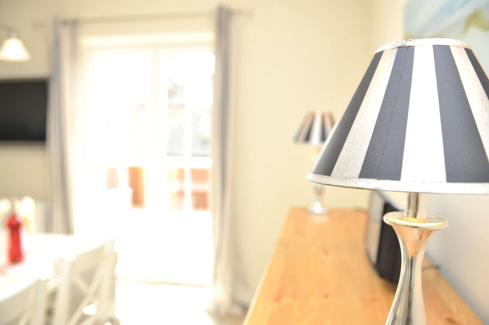 Tischlampe mit schwarz-weißem Schirm auf Holztisch. Im Hintergrund Tür und Stuhl.