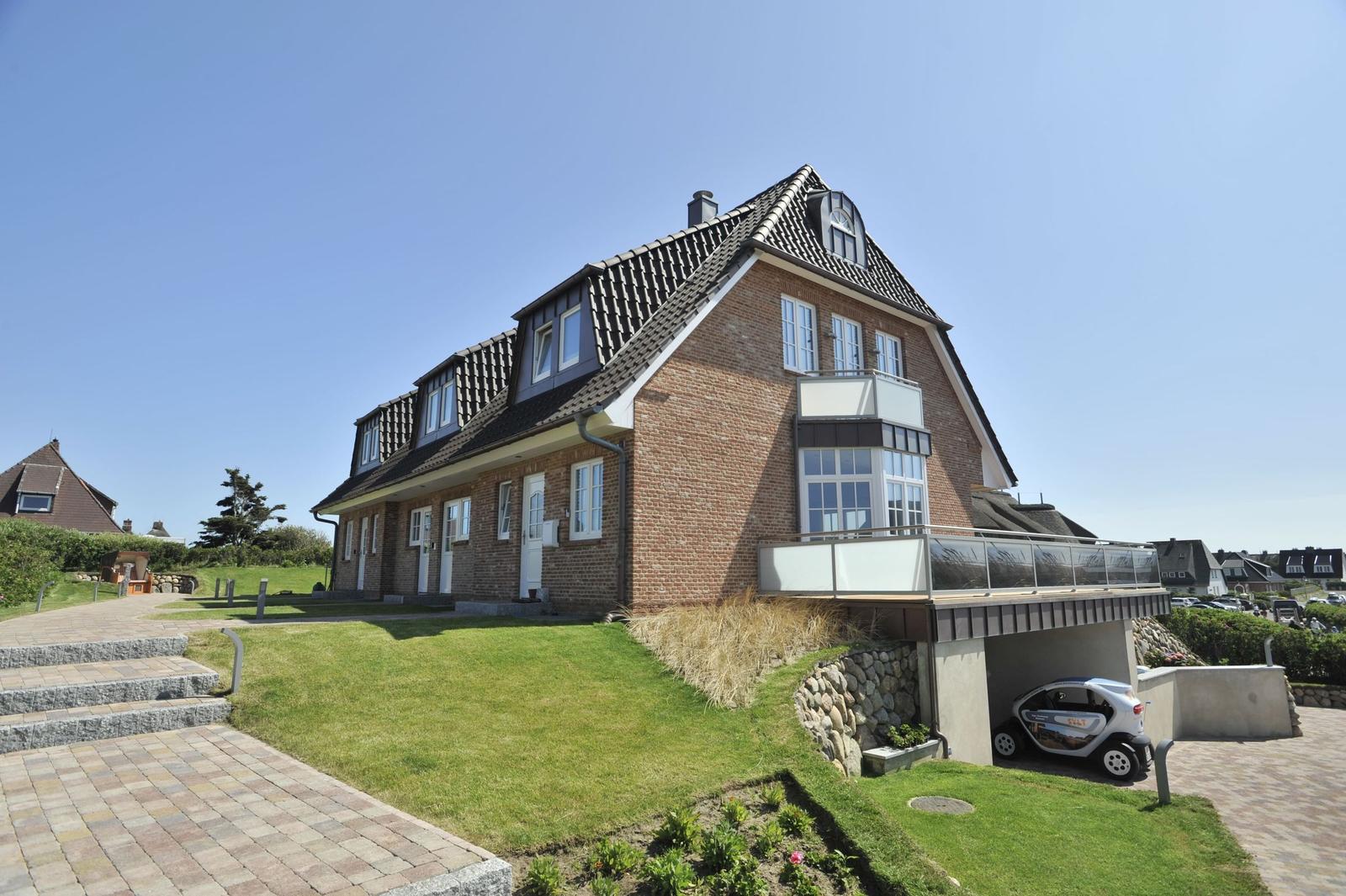 Ein zweistöckiges Haus mit Balkon und Garage. Grasfläche und gepflasterte Wege.