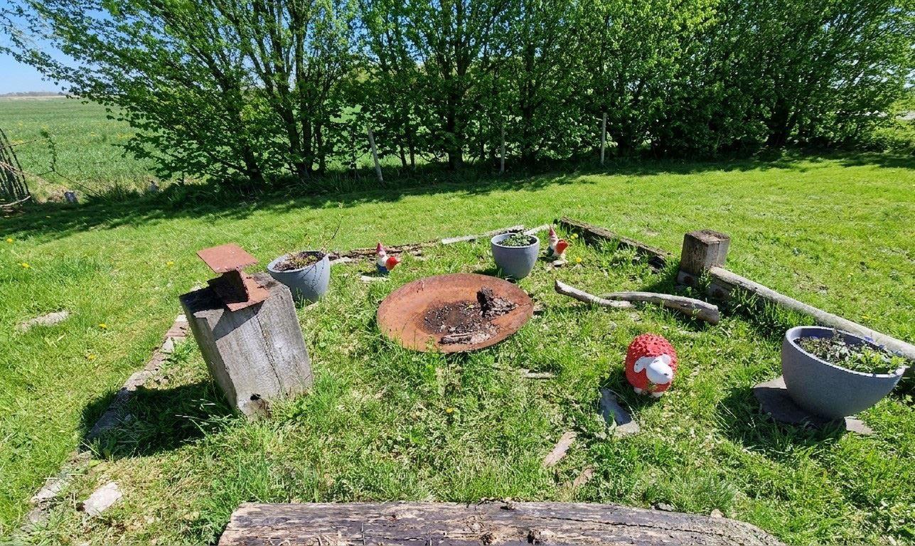 Grüner Garten mit Feuerstelle, Pflanzkübel und dekorativen Figuren.