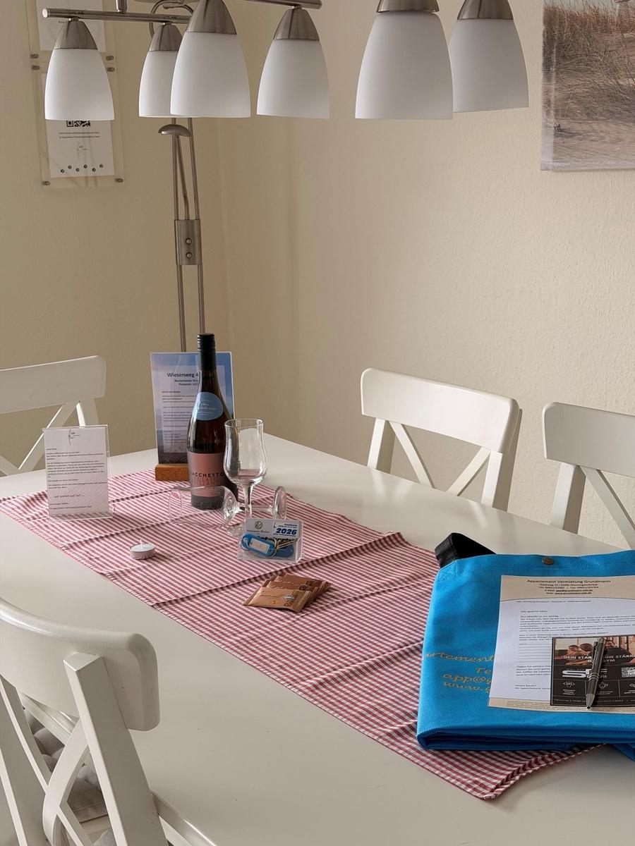 Esstisch mit Stühlen, Tischdecke, Weinflasche und Gläser.
