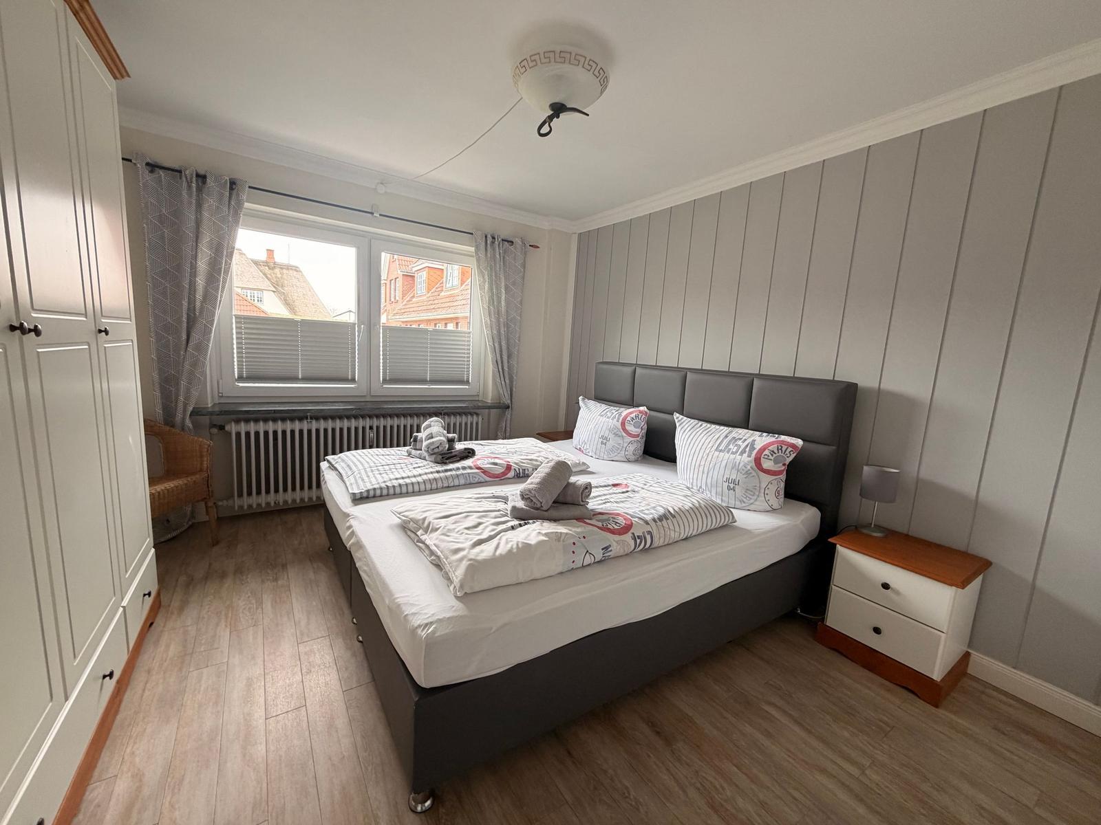 Schlafzimmer mit Doppelbett, Kleiderschrank und Fenster mit Blick auf Dächer.