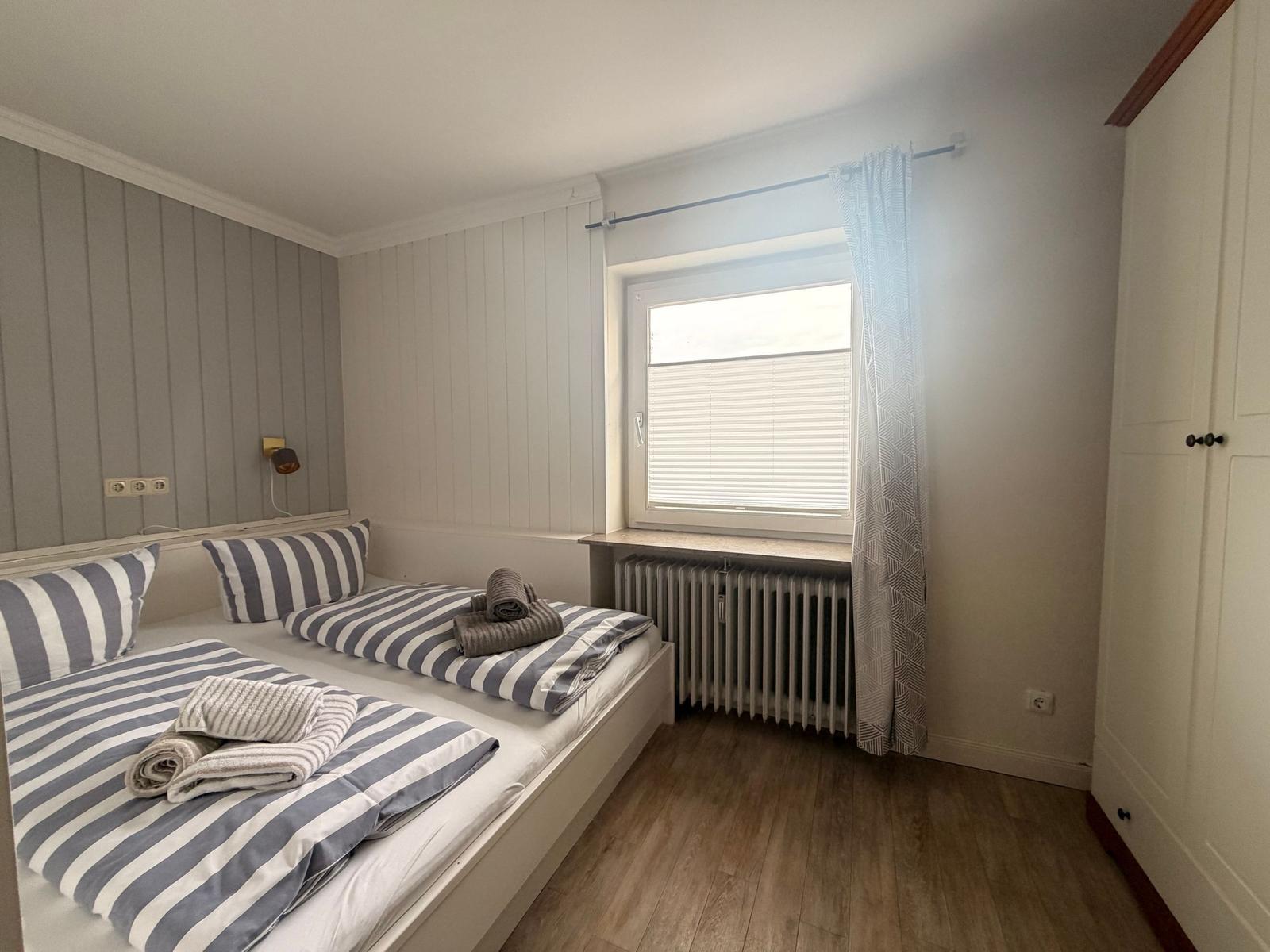Zimmer mit Doppelbett, Fenster und Kleiderschrank.
