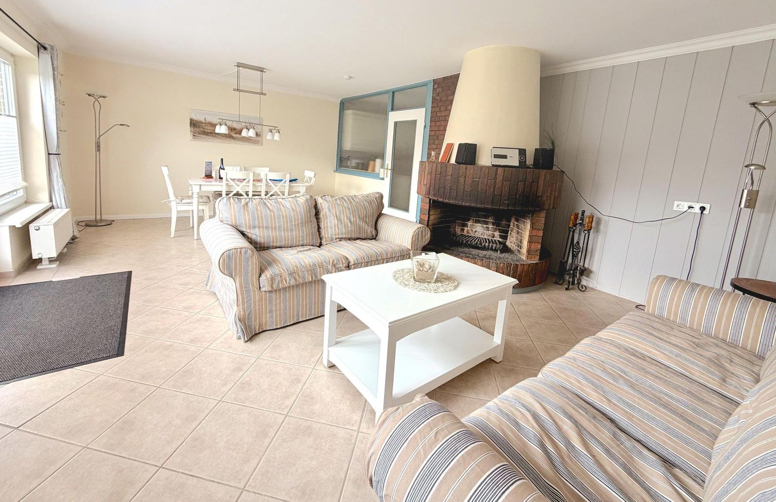 Wohnzimmer mit Sofa, Kamin und Essbereich im Hintergrund.