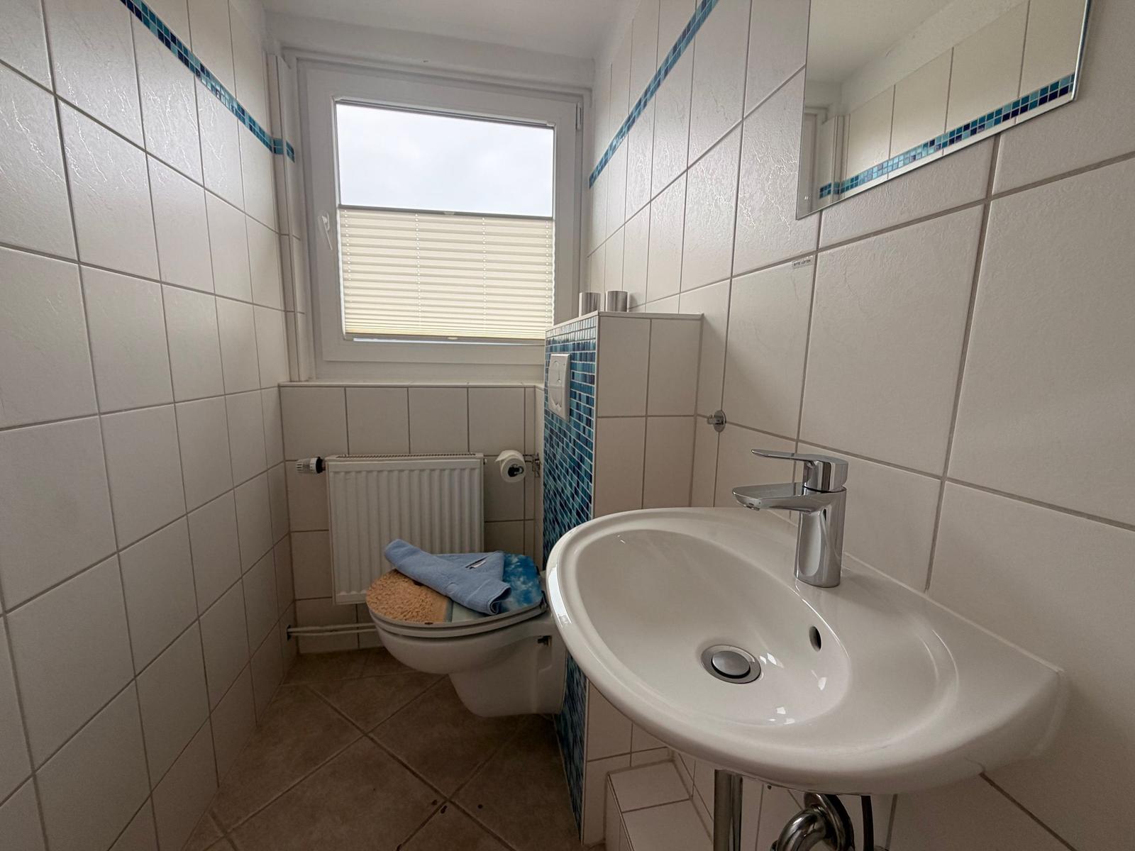 Badezimmer mit Waschbecken, Spiegel, Toilette und Fenster
