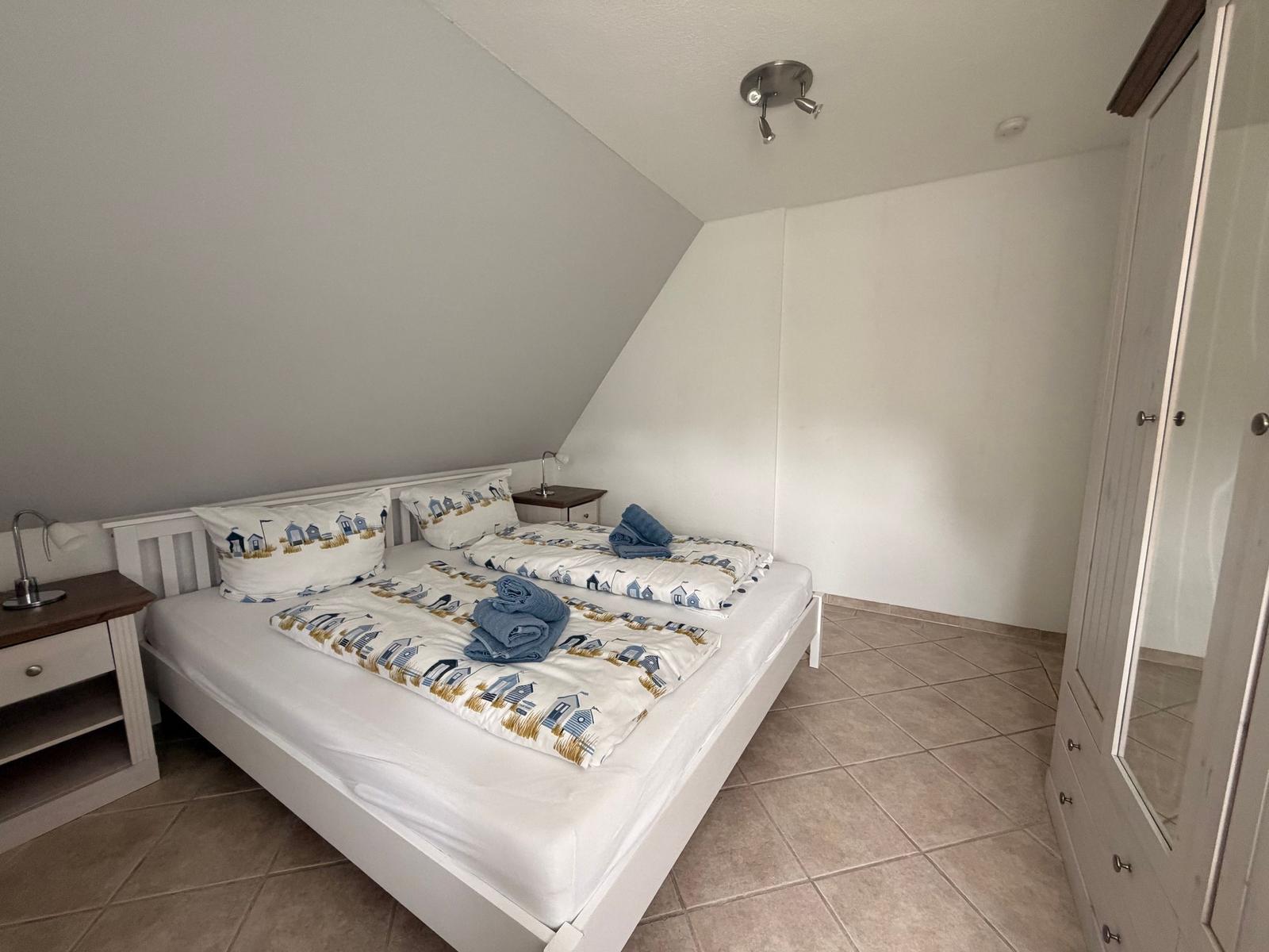 Schlafzimmer mit Doppelbett, Nachttisch und Kleiderschrank unter schräger Decke.