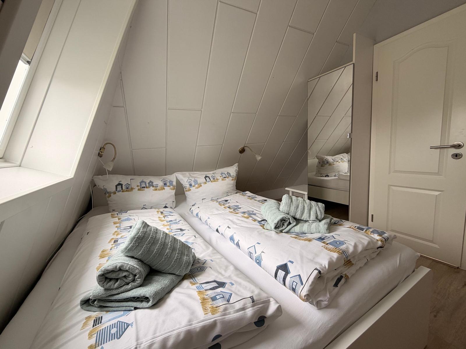 Zimmer mit zwei Betten, Spiegeltüren und Dachschrägen.