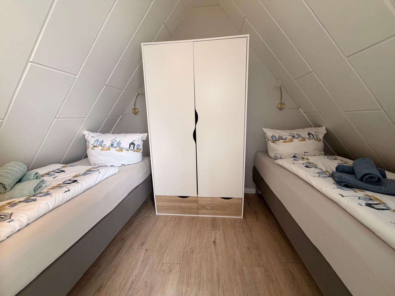 Zwei Betten und ein Schrank in einem Dachzimmer mit Holzboden.