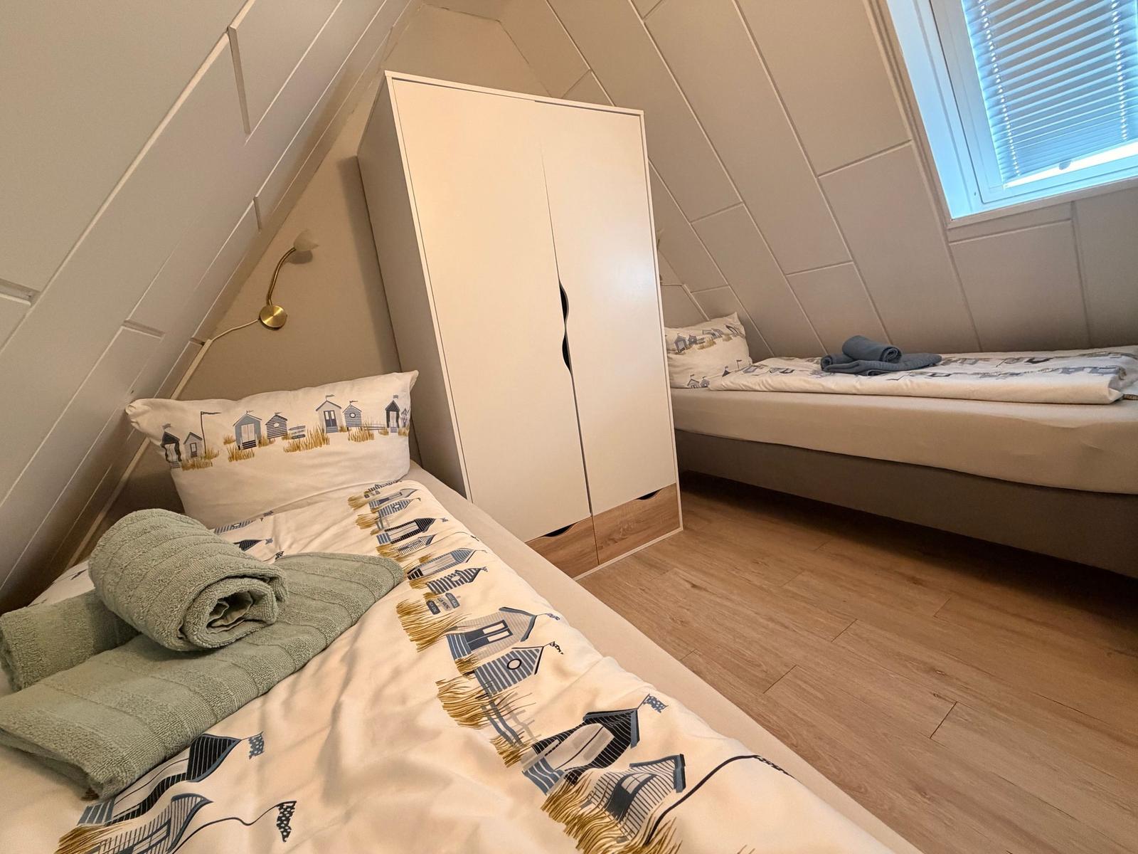 Zwei Betten mit Strandmotiv in einem Dachzimmer mit Holzboden und Fenster.