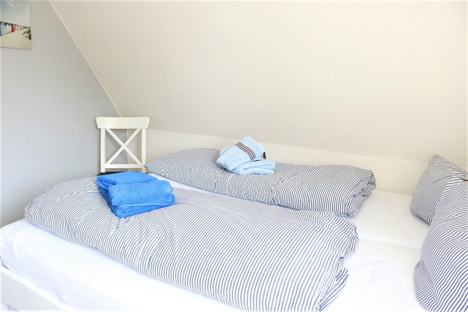 Schlafzimmer mit Doppelbett, gestreifter Bettwäsche und blauen Handtüchern.