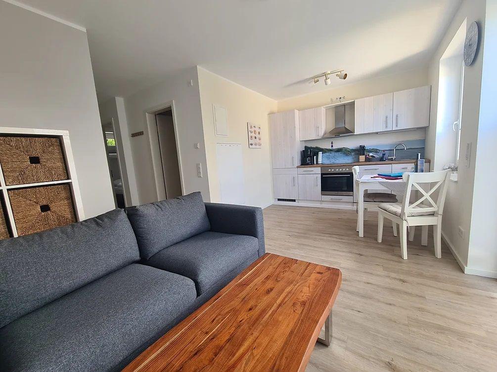 Wohn- und Küchenbereich mit Sofa, Tisch und weißen Schränken.