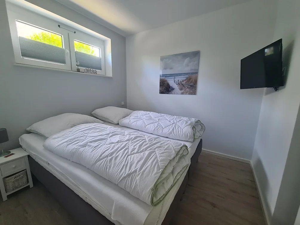 Schlafzimmer mit Doppelbett, Wandbild und Fernseher.