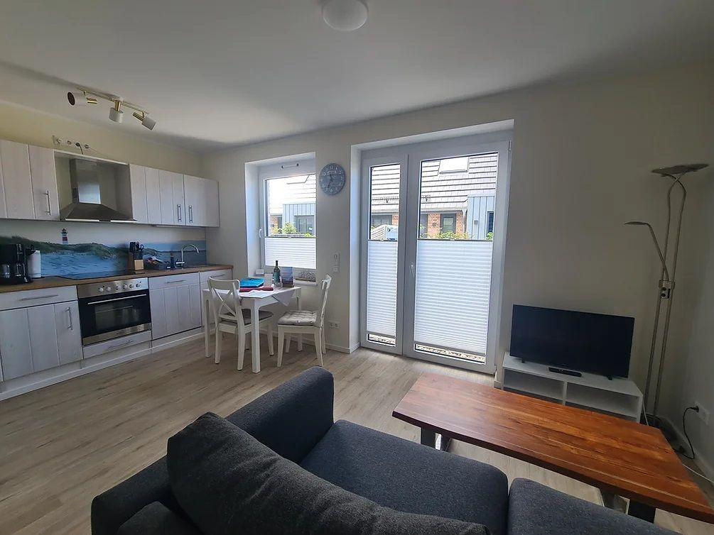 Wohnküche mit Essbereich, Sofa und TV. Glastür führt auf Balkon.