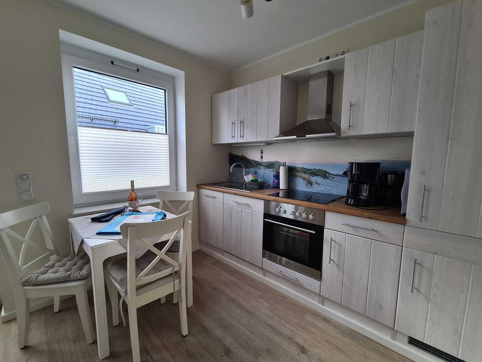 Küche mit Essbereich, hellen Schränken und Küchenzeile mit Herd und Spüle.