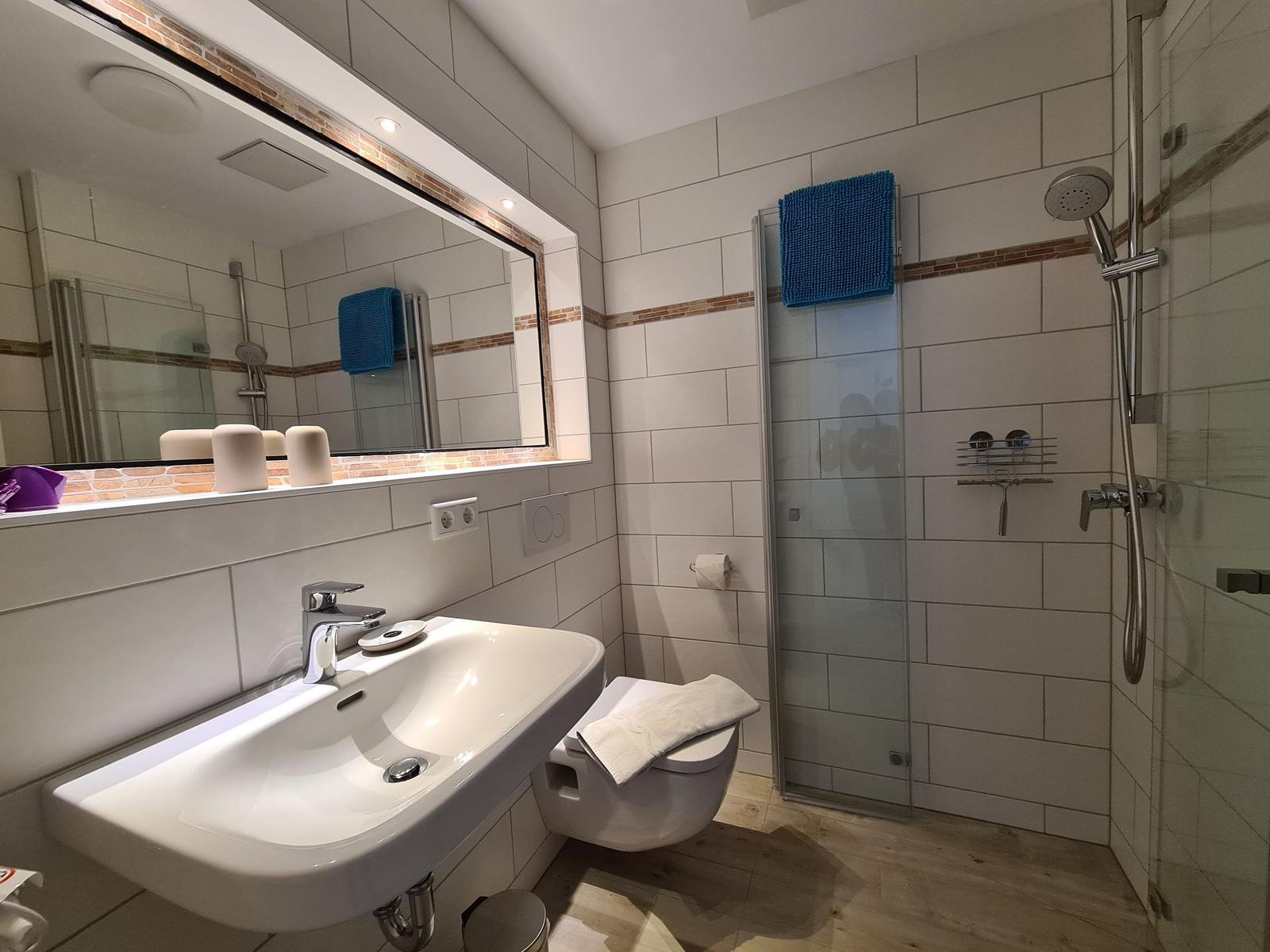 Badezimmer mit Dusche, Waschbecken und Toilette. Fliesenwand mit blauem Handtuch.