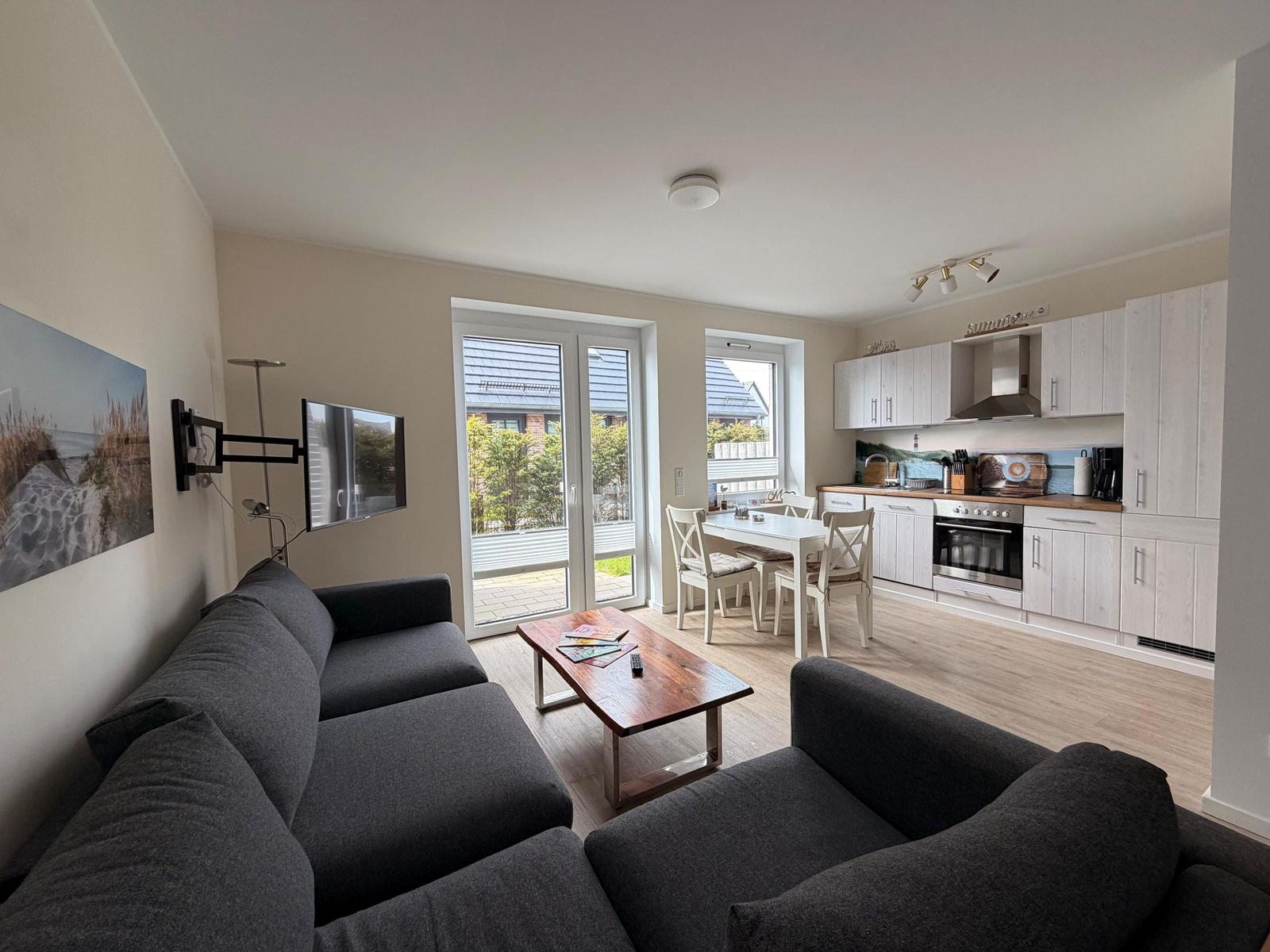 Wohnzimmer mit Sofa, Couchtisch und TV. Küche mit Esstisch und Fenster.