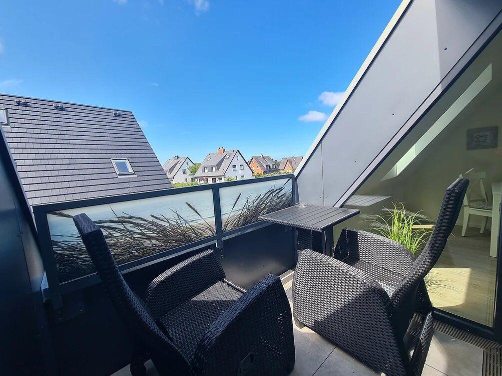 Terrace with two chairs and table, view of roofs and sky.