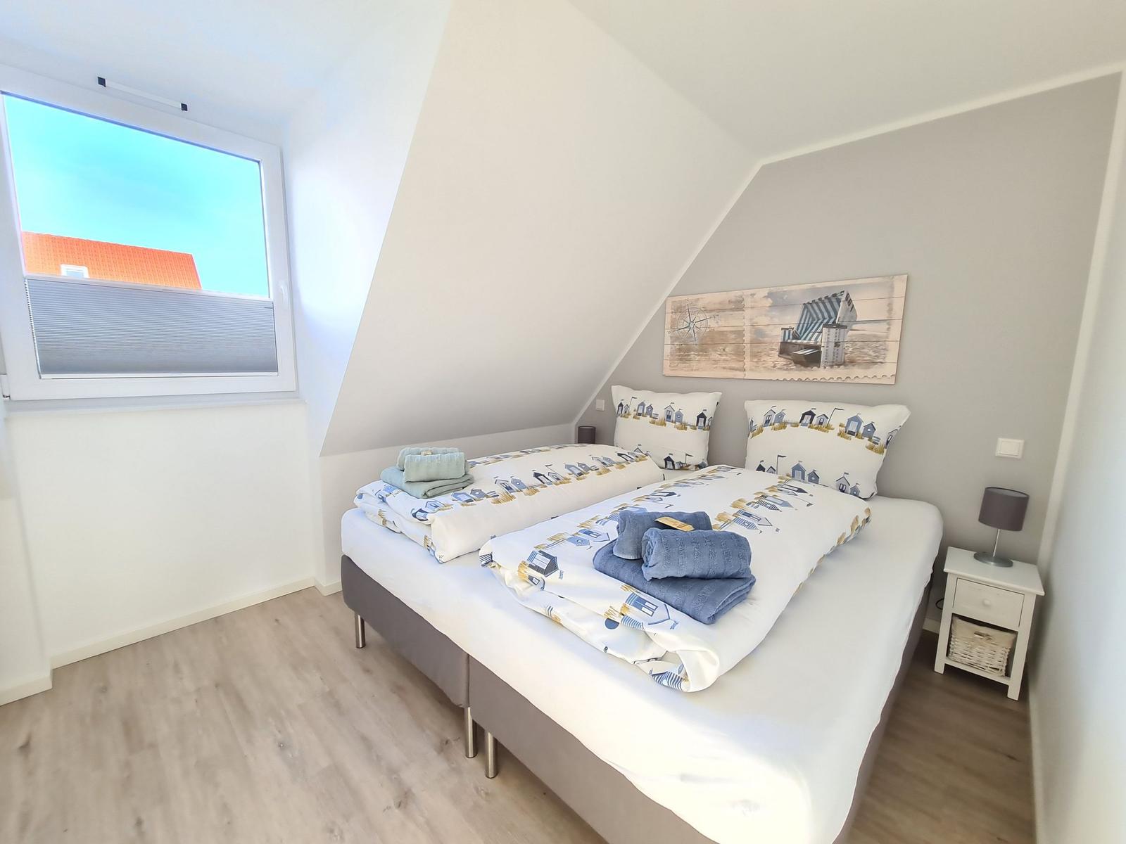 Schlafzimmer mit Doppelbett, Fenster und Nachttisch.