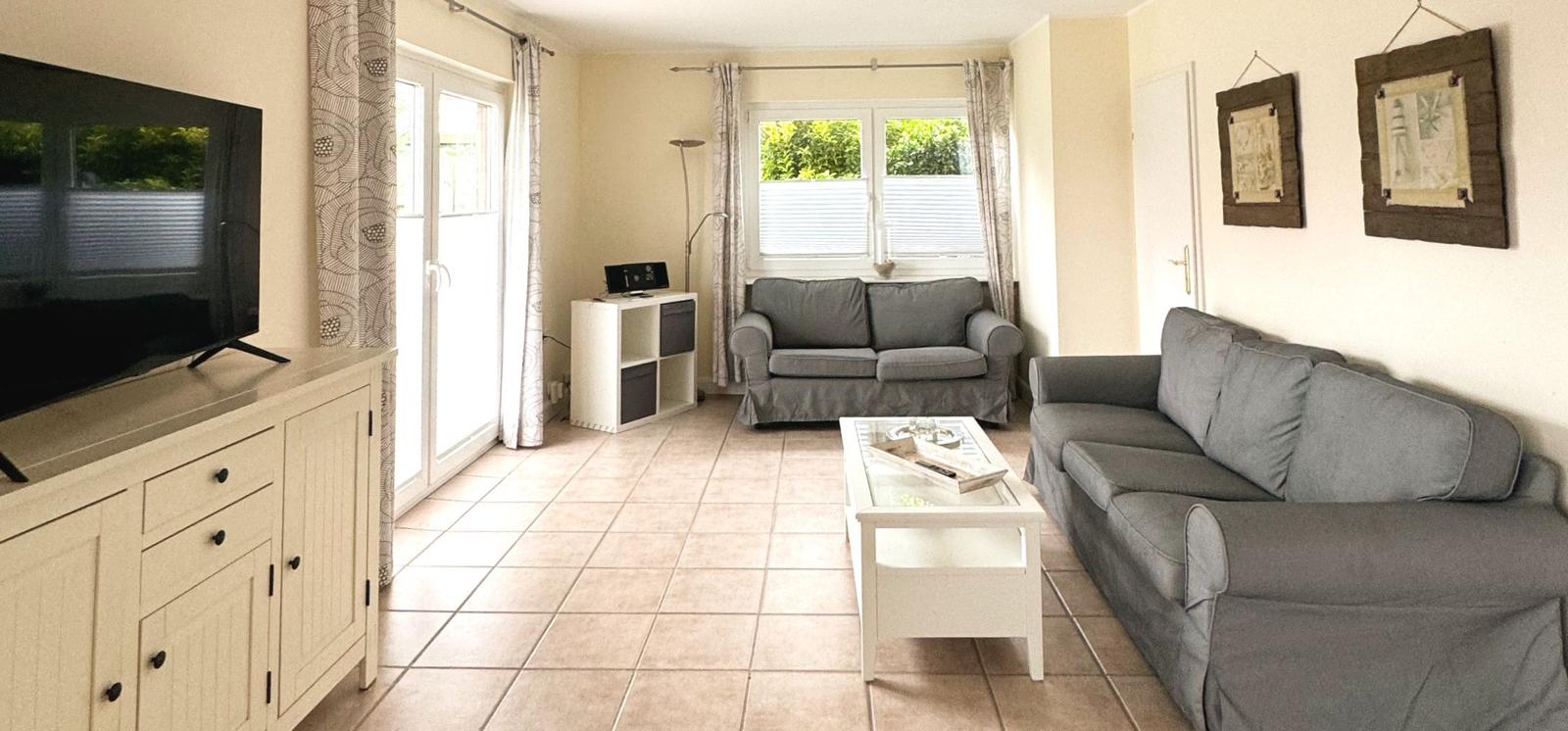 Wohnzimmer mit zwei grauen Sofas, Glas-Tisch und TV auf Sideboard.