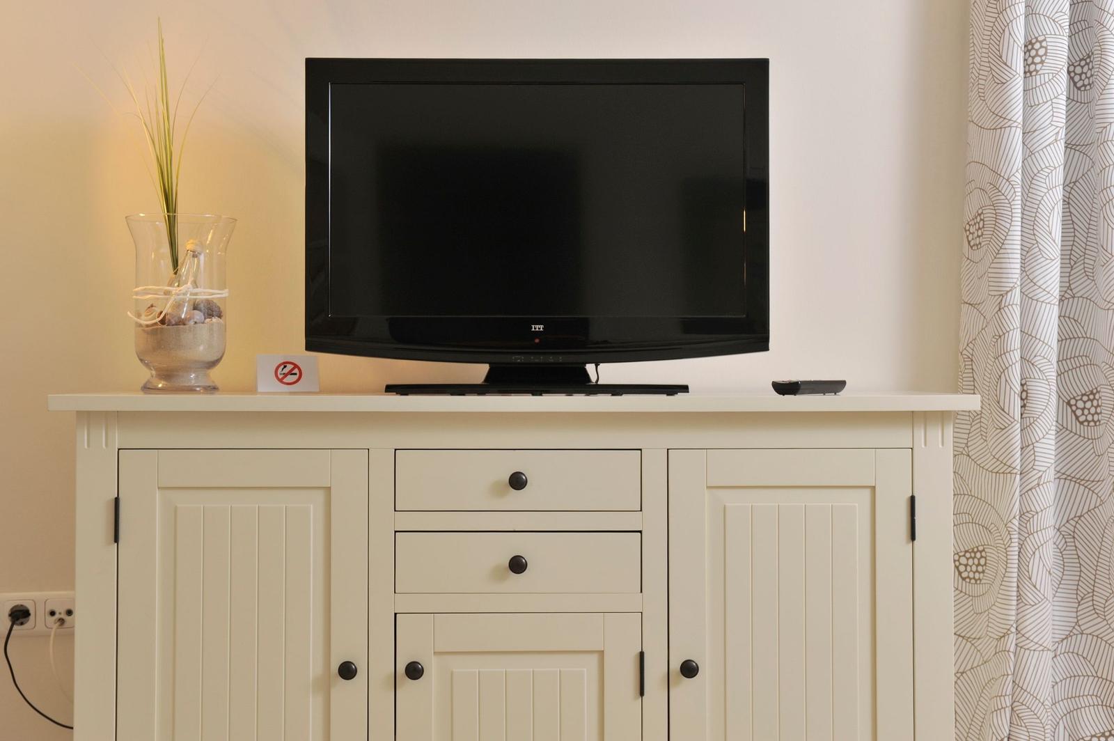 Flachbildfernseher auf einem weißen Schrank mit Schubladen und Türen.