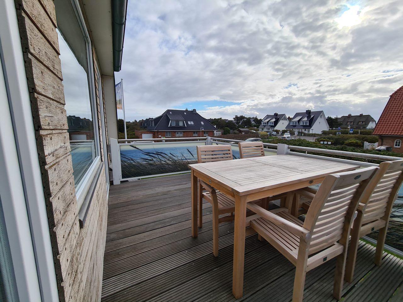 Terrasse mit Holztisch und Stühlen, Blick auf Häuser und Wasser.