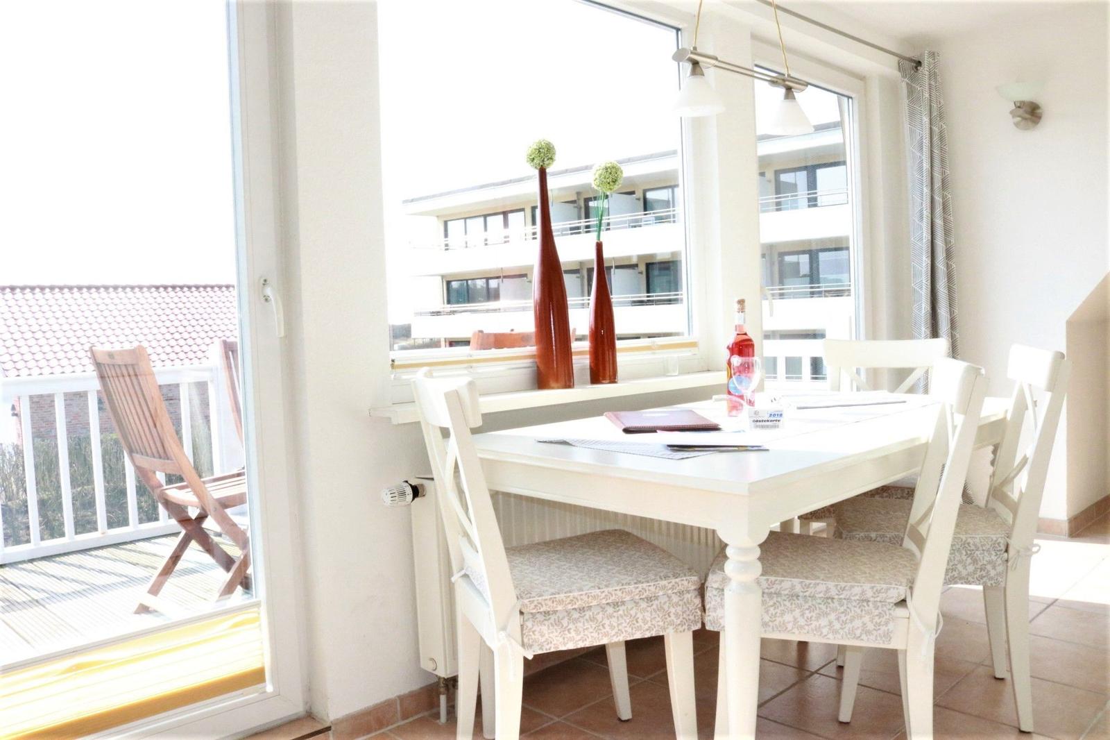 Esszimmer mit weißem Tisch und Stühlen, Blick auf Balkon und Gebäude.