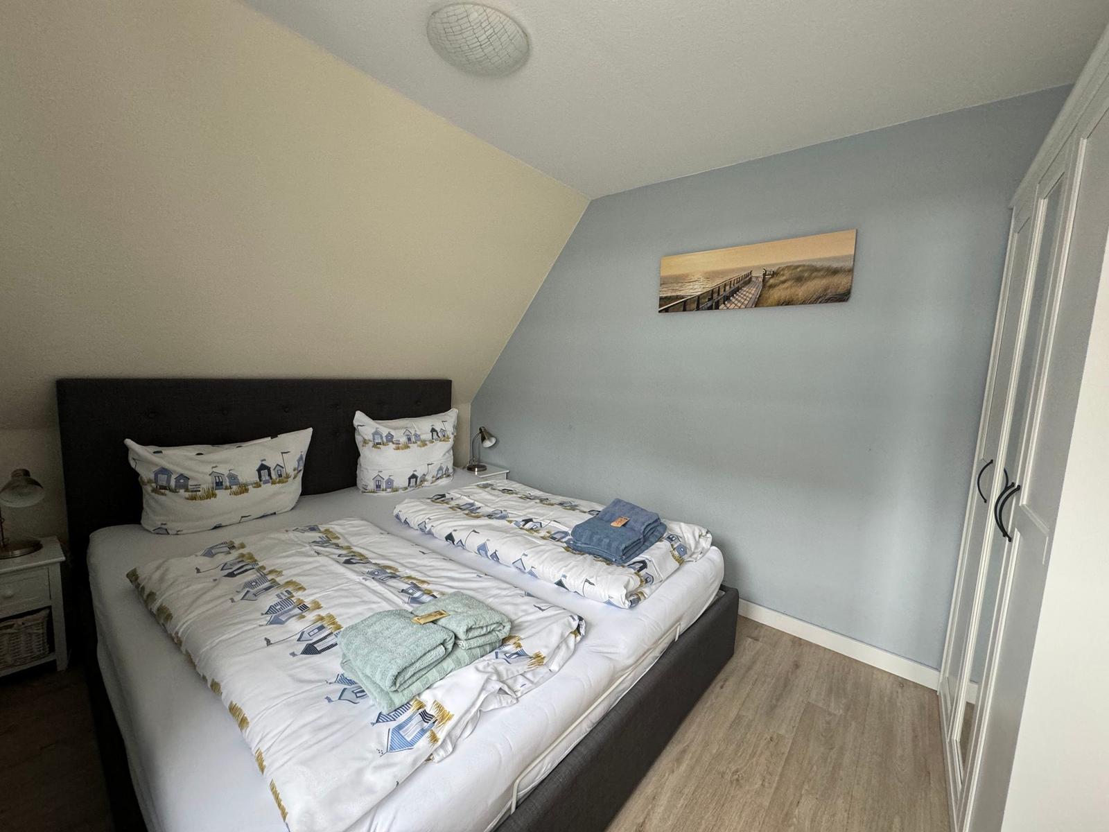 Schlafzimmer mit Doppelbett, Wandbild und Kleiderschrank.