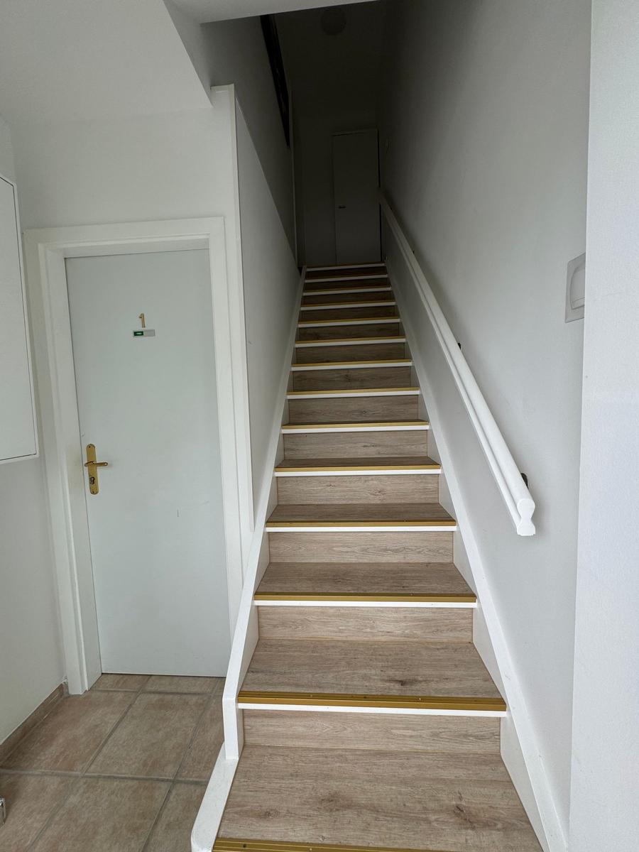 Treppenhaus mit Holztreppe und weißen Wänden. Tür mit goldenem Griff.