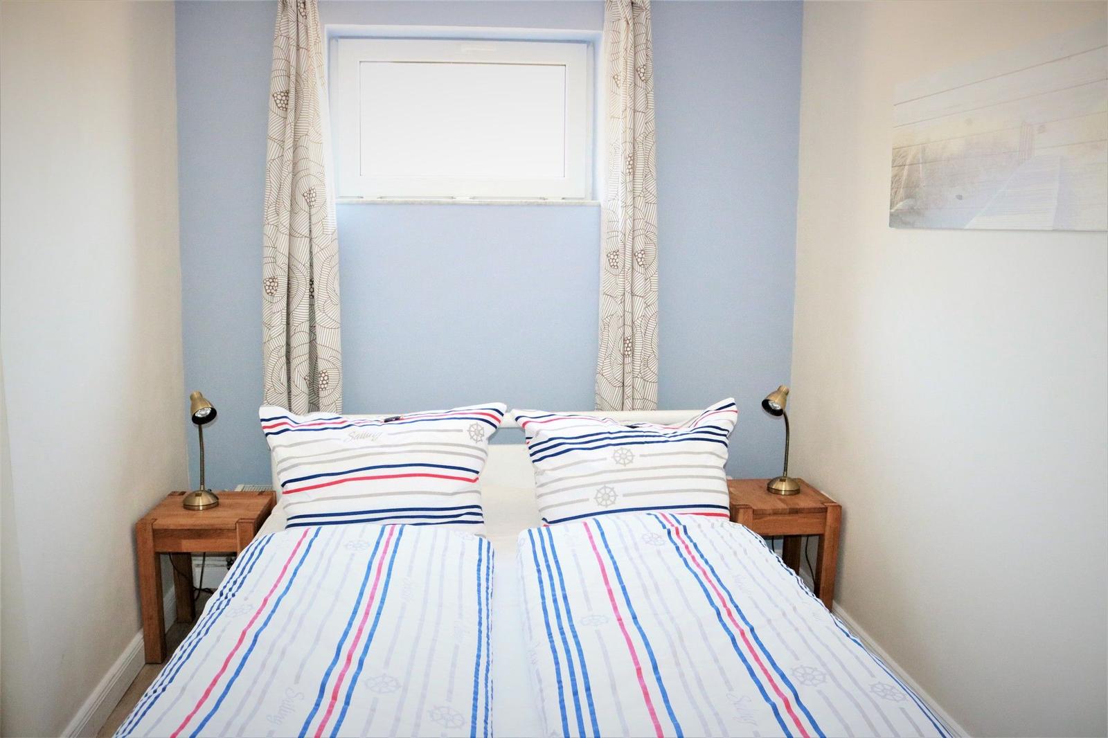 Two beds with striped bed linen, nightstands with lamps, and window with curtains.
