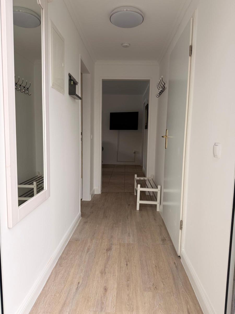 Hallway with wooden floor, mirror, hooks, and bench.