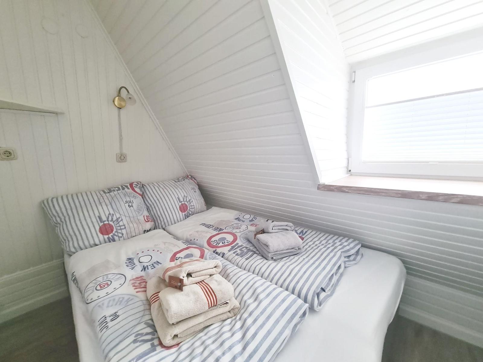 Double bed with linens and towels under sloped ceiling with window.