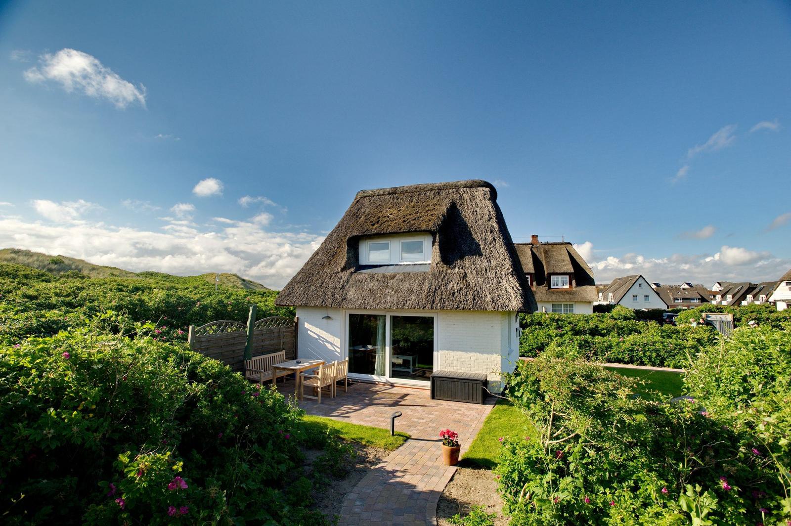 House with thatched roof, terrace, and garden. View of dunes and neighboring houses.