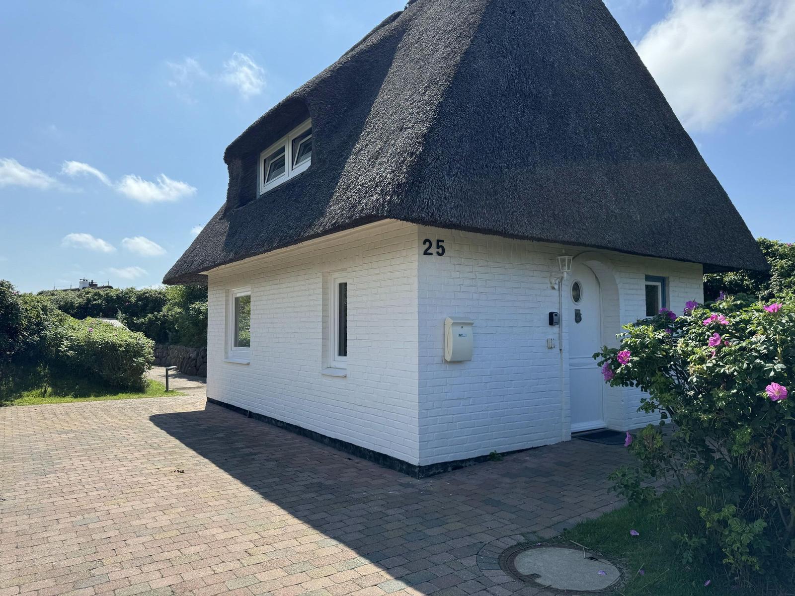 Weißes Haus mit Strohdach, Eingangstür und Blumenbeet