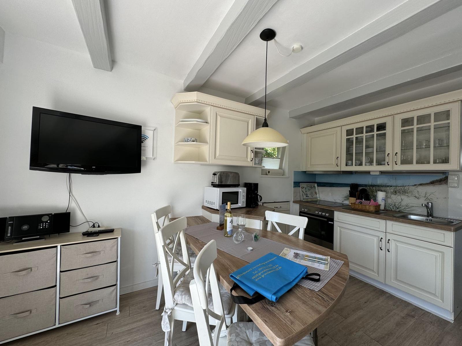 Küche mit Esstisch, weißen Schränken und TV an der Wand.