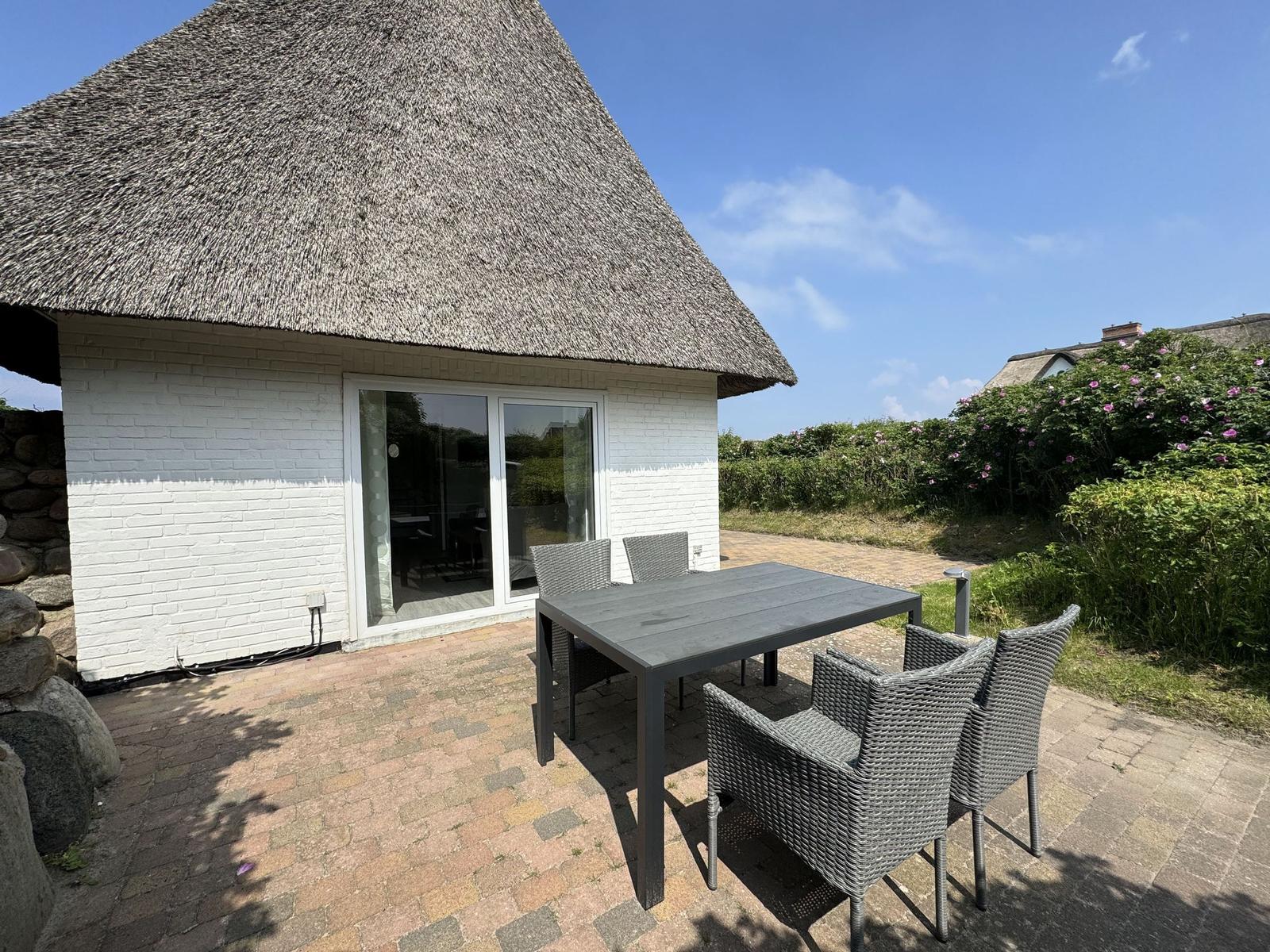 Terrasse mit Tisch und Stühlen vor einem Haus mit Strohdach.