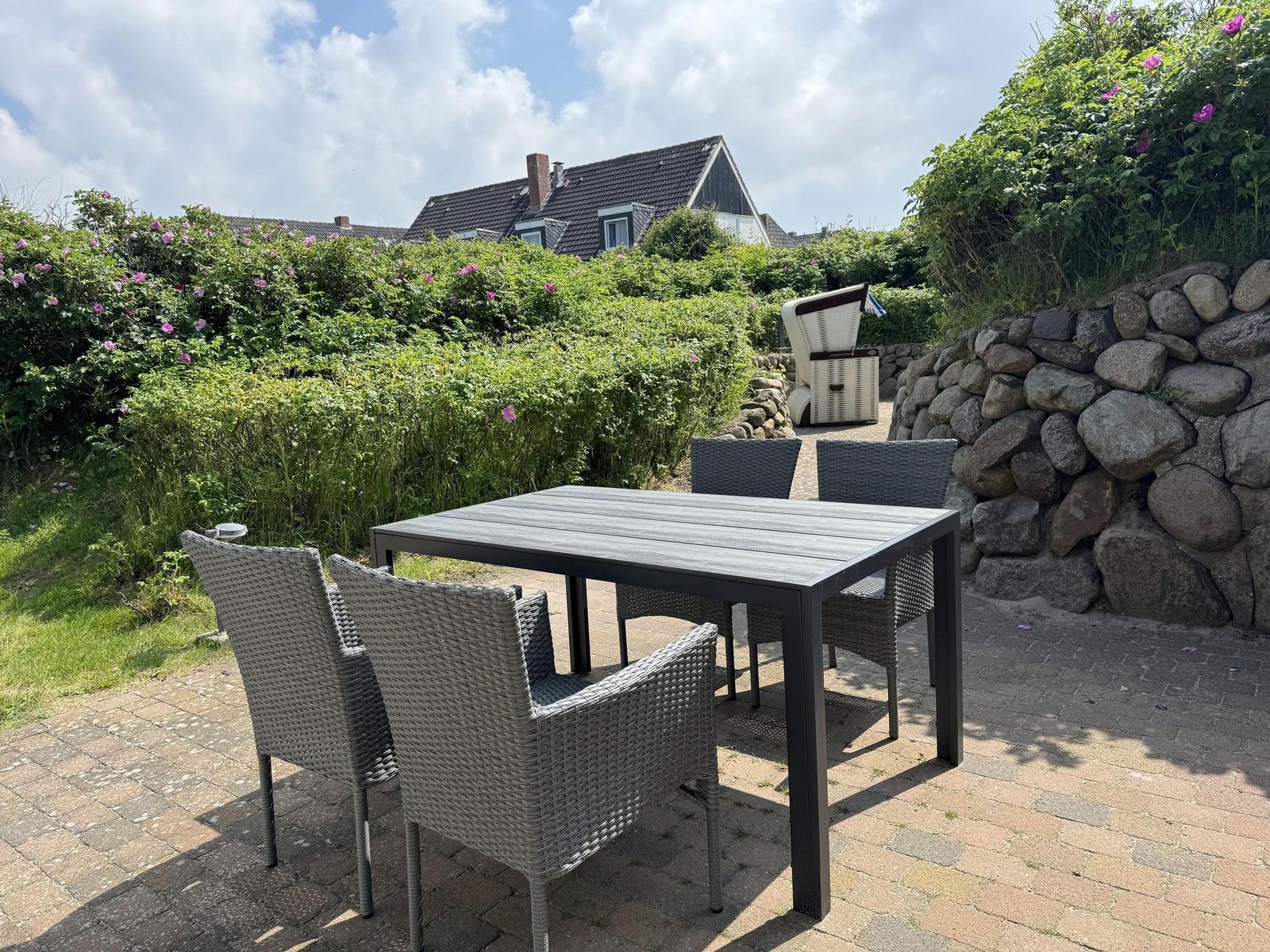 Terrasse mit Tisch und Stühlen, umgeben von Grün und Steinmauer.