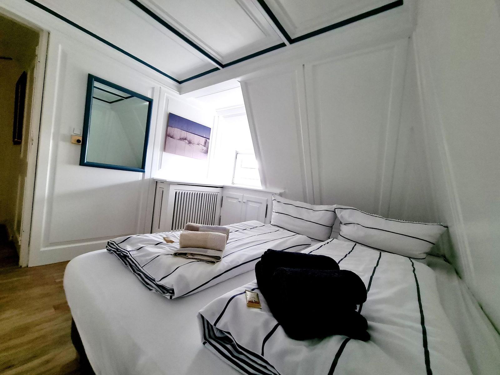 Schlafzimmer mit Bett, Spiegel und Fenster. Dachbodenraum mit weißen Wänden.